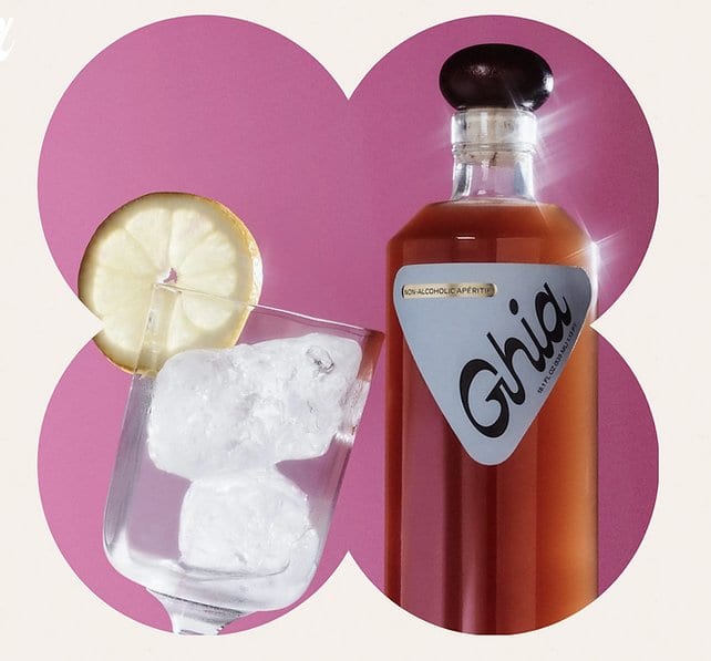 A glass with ice and lemon slice leaning against a bottle