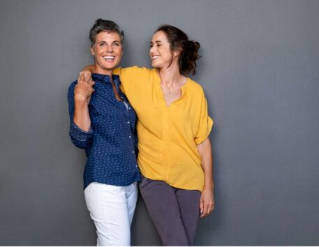 iStock-1180926158-min-2048x1588-1 two women with their arms around each other. One is smiling at the other, the other is smiling at the camera.